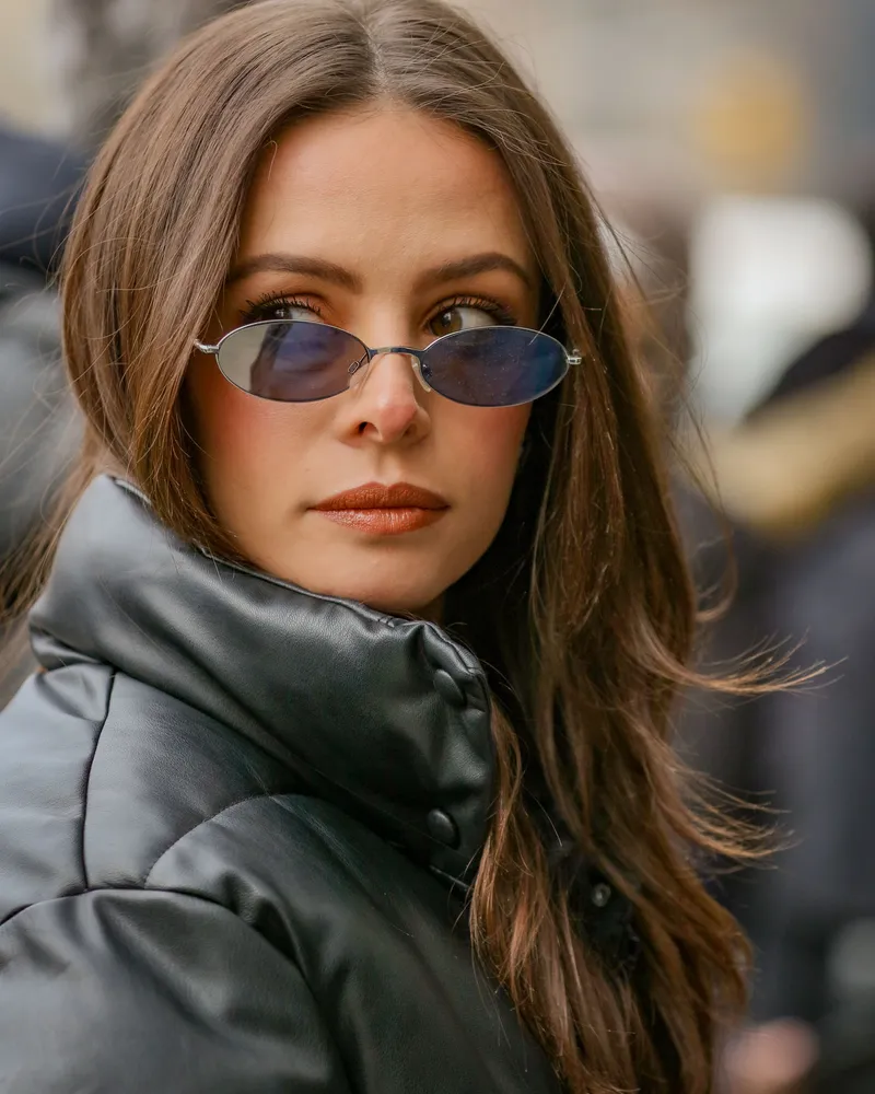 Close-up of a model in a black leather-look puffer jacket with a tall storm collar and matte snap hardware.