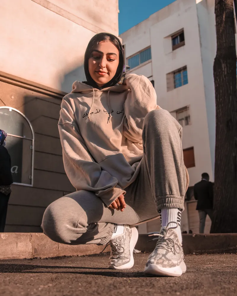 A model crouching in a beige fleece hoodie and matching grey joggers with elastic cuffs.