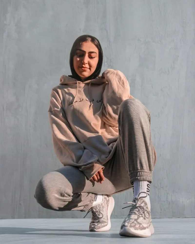 A model crouching in a tan fleece hoodie with front script print and matching tapered joggers.