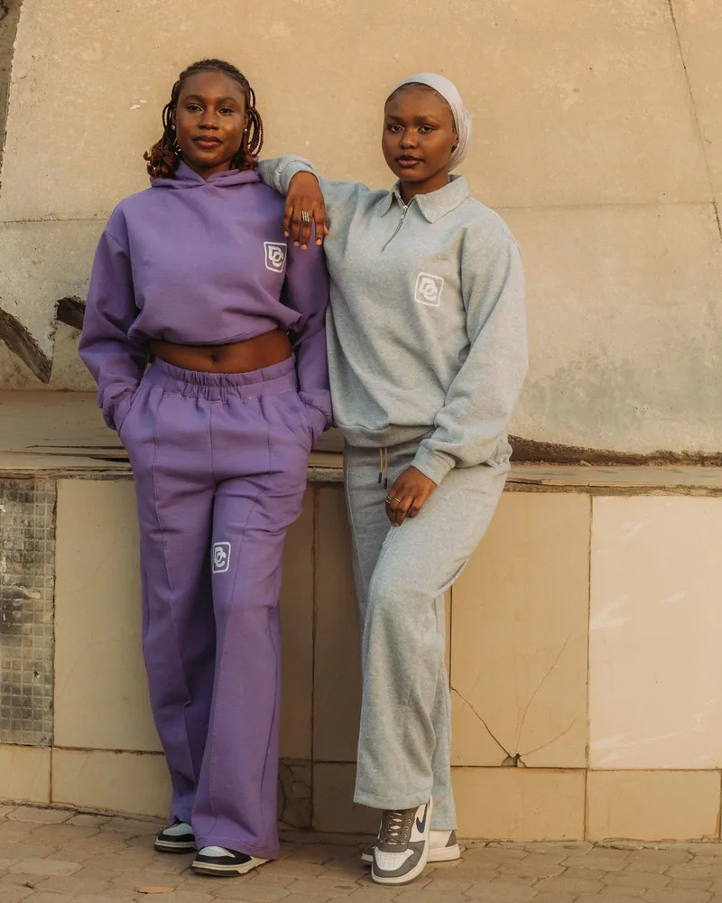 Two models in matching brushed-fleece tracksuits, purple and grey, each with a small embroidered chest logo.