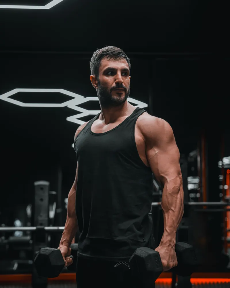 A model in a black ribbed training tank top, gym setting.